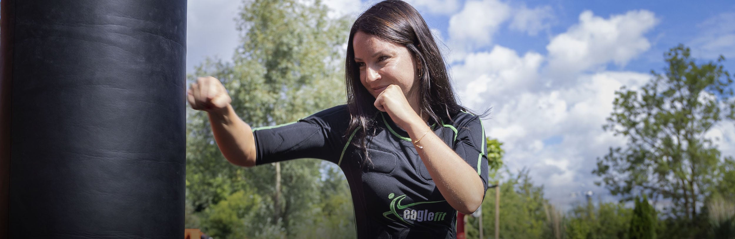 Person im EMS-Anzug trainiert in einem Outdoor-Gym an einem Boxsack