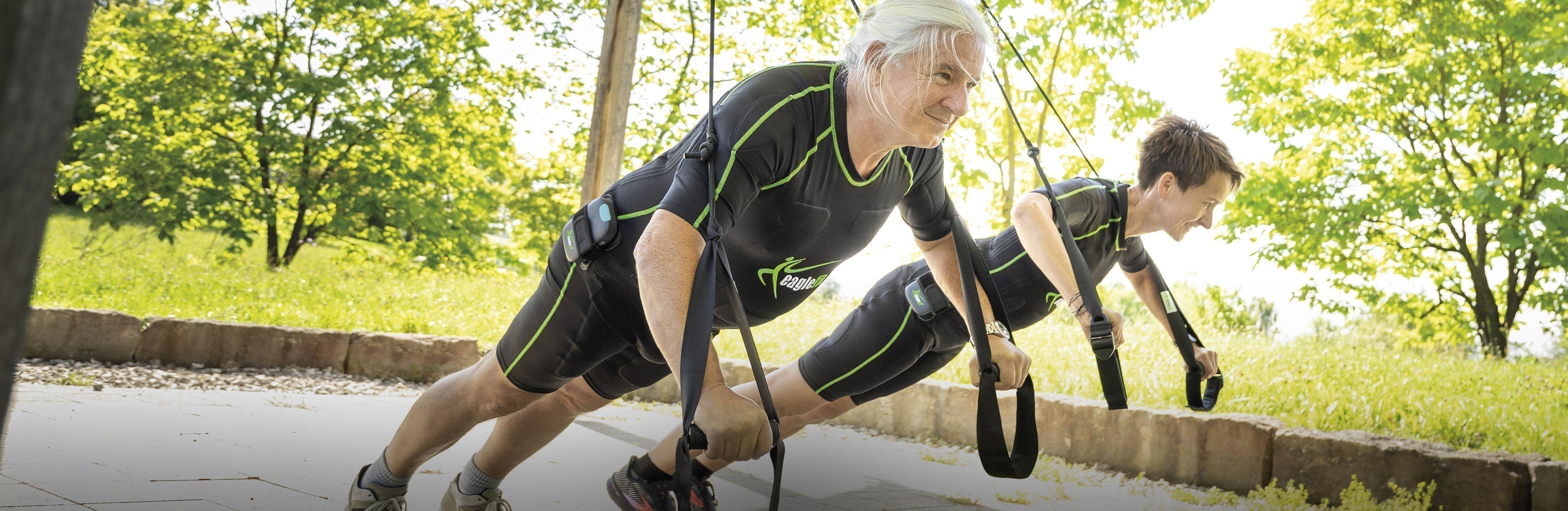 Zwei Personen in EMS-Anzügen trainieren mit Sling-Trainer