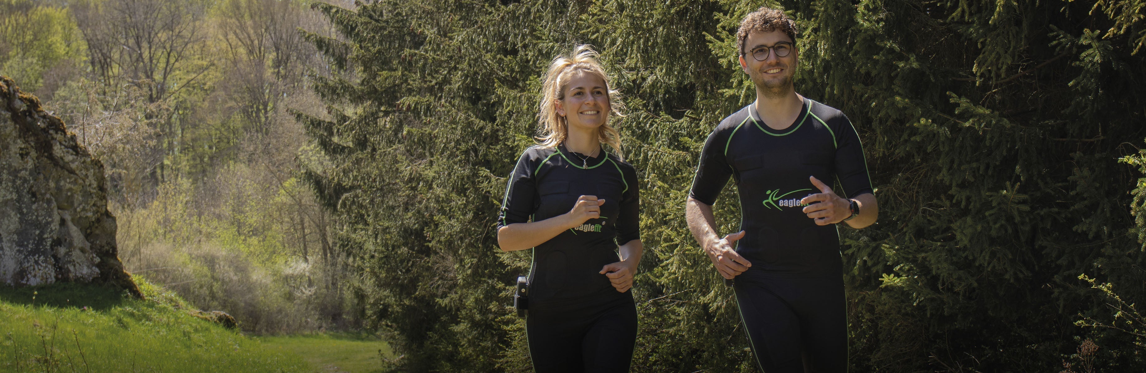 Zwei Personen in EMS-Anzügen joggen durch die Natur